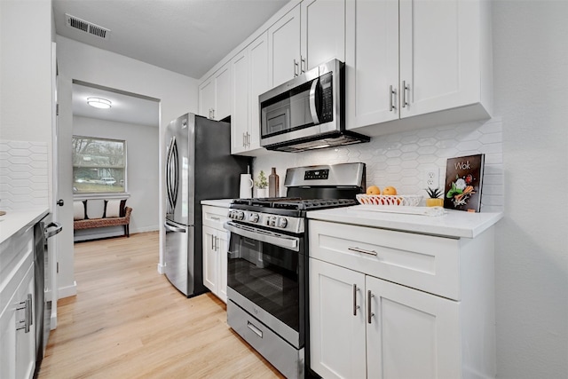 kitchen with light hardwood / wood-style flooring, stainless steel appliances, light stone counters, decorative backsplash, and white cabinets