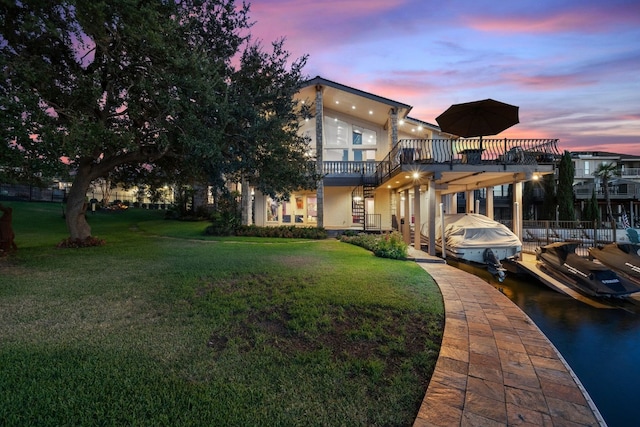 back house at dusk featuring a balcony and a lawn