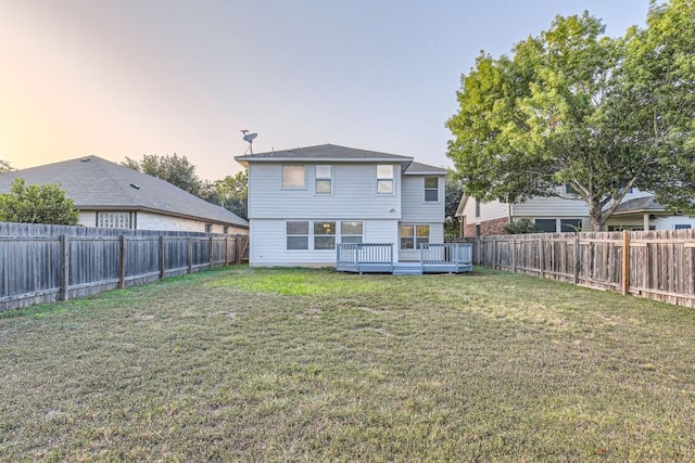 back house at dusk featuring a wooden deck and a yard