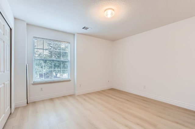 empty room with a textured ceiling and light hardwood / wood-style floors