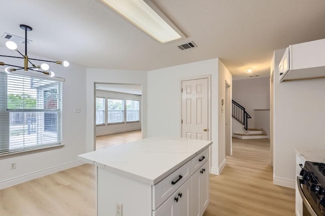 kitchen featuring white cabinetry, light hardwood / wood-style flooring, stainless steel range with gas cooktop, pendant lighting, and light stone countertops