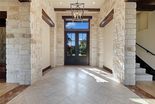 tiled foyer entrance featuring a towering ceiling, french doors, beam ceiling, and an inviting chandelier