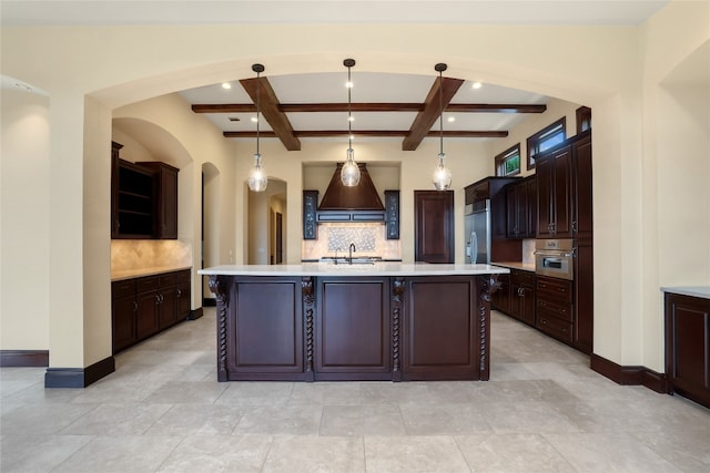 kitchen featuring backsplash, hanging light fixtures, an island with sink, and beamed ceiling