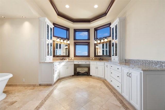 bathroom with a tray ceiling, vanity, a bathing tub, and crown molding