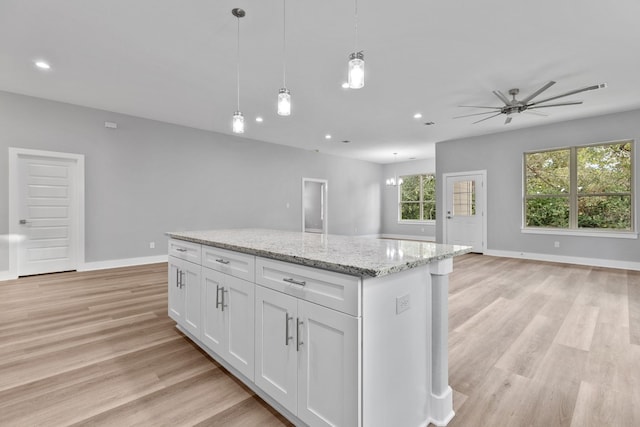 kitchen featuring white cabinetry, hanging light fixtures, light stone countertops, a kitchen island, and light wood-type flooring