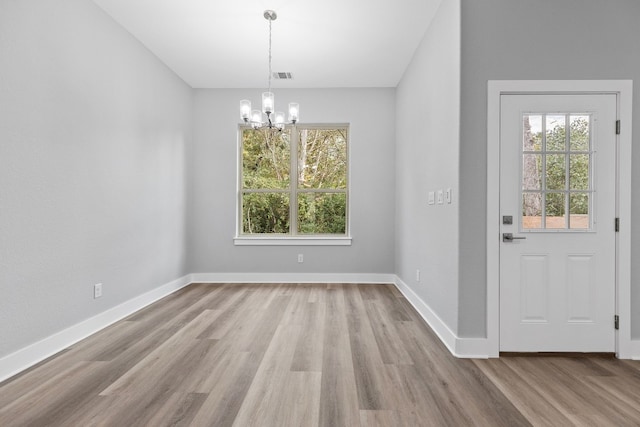 unfurnished dining area with plenty of natural light, a notable chandelier, and light hardwood / wood-style flooring