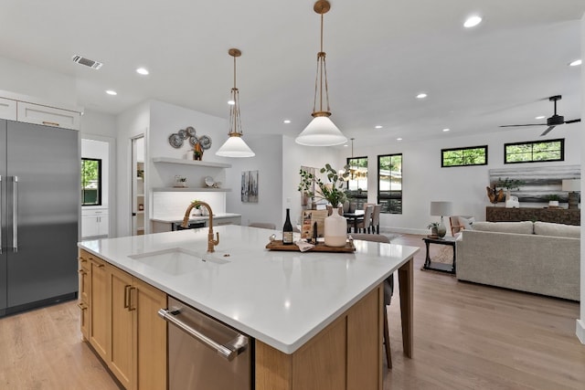 kitchen featuring decorative light fixtures, sink, a large island with sink, stainless steel appliances, and light wood-type flooring