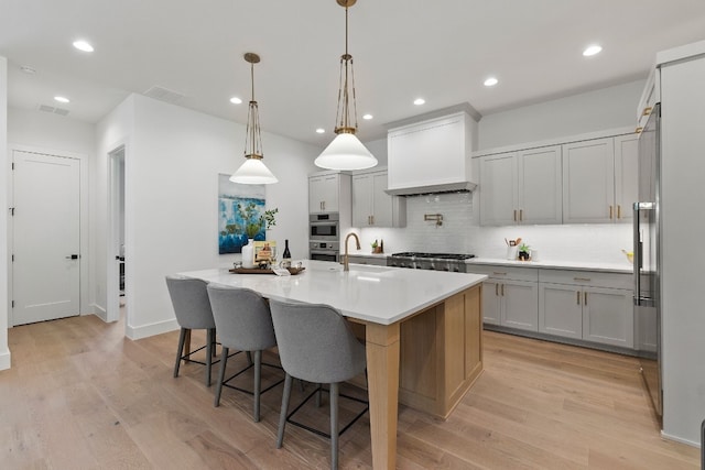 kitchen featuring a spacious island, sink, decorative light fixtures, light hardwood / wood-style flooring, and custom range hood