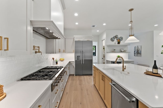 kitchen with premium range hood, sink, white cabinetry, appliances with stainless steel finishes, and pendant lighting