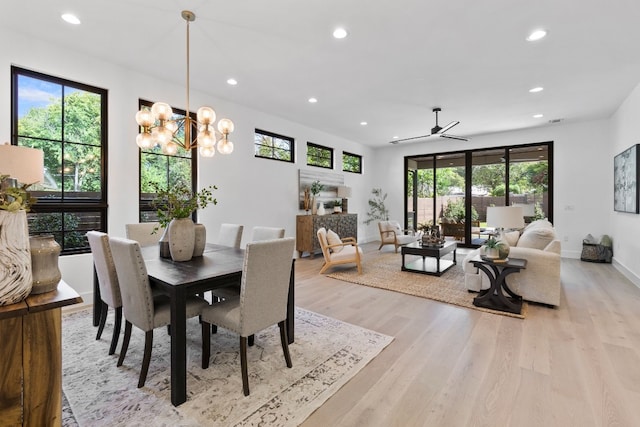 dining space with ceiling fan with notable chandelier and light wood-type flooring