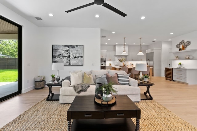 living room with wine cooler, ceiling fan, and light hardwood / wood-style flooring