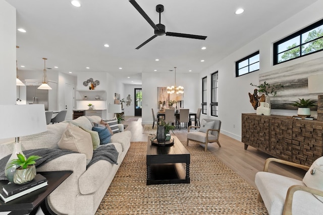 living room featuring ceiling fan with notable chandelier and light hardwood / wood-style flooring