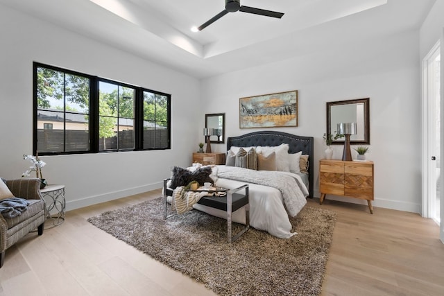 bedroom featuring ceiling fan, a raised ceiling, and light wood-type flooring