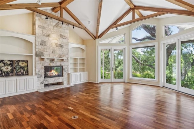 unfurnished living room with beam ceiling, built in features, hardwood / wood-style floors, a stone fireplace, and high vaulted ceiling