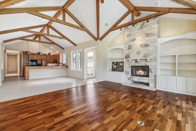 unfurnished living room with built in shelves, beam ceiling, a stone fireplace, and high vaulted ceiling