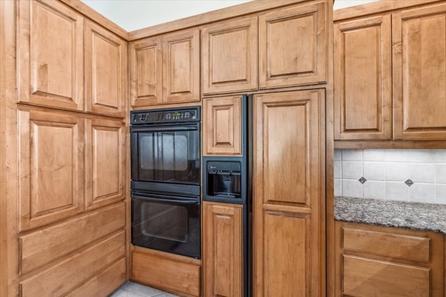 kitchen with dark stone counters, double oven, paneled built in refrigerator, and backsplash