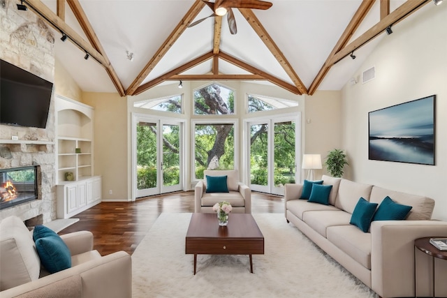 living room with hardwood / wood-style flooring, beam ceiling, a stone fireplace, and high vaulted ceiling