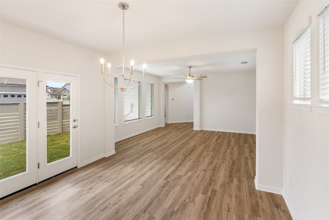 unfurnished dining area featuring ceiling fan with notable chandelier, light wood-type flooring, and a wealth of natural light