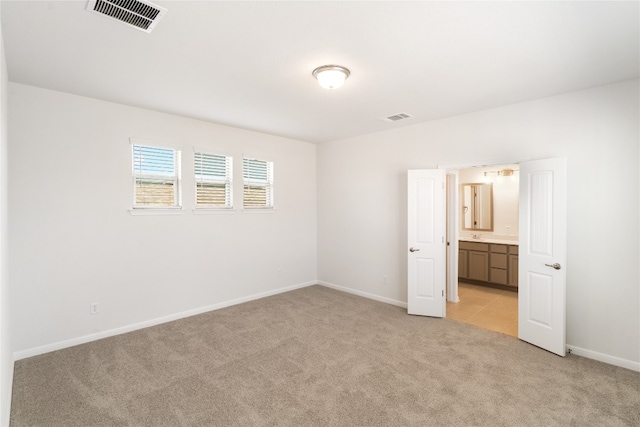 unfurnished bedroom featuring light carpet and ensuite bathroom