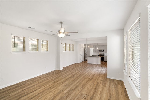 unfurnished living room with ceiling fan with notable chandelier, light wood-type flooring, and plenty of natural light