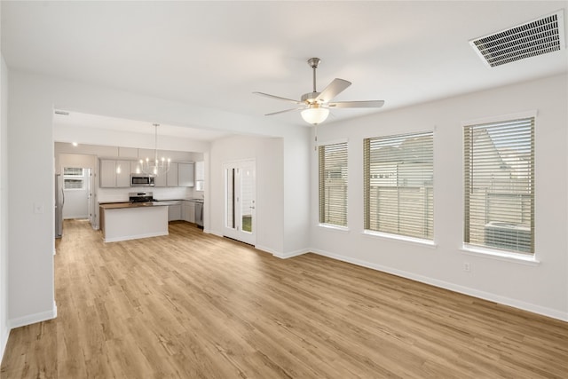 unfurnished living room featuring ceiling fan with notable chandelier, light hardwood / wood-style flooring, and a healthy amount of sunlight