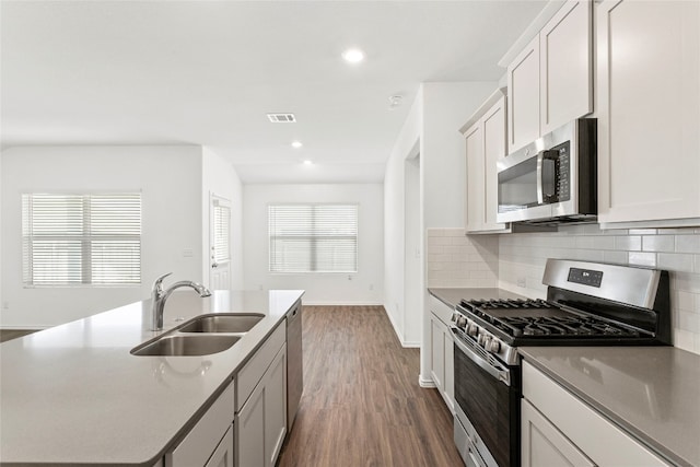 kitchen featuring appliances with stainless steel finishes, dark wood-type flooring, sink, a center island with sink, and white cabinets