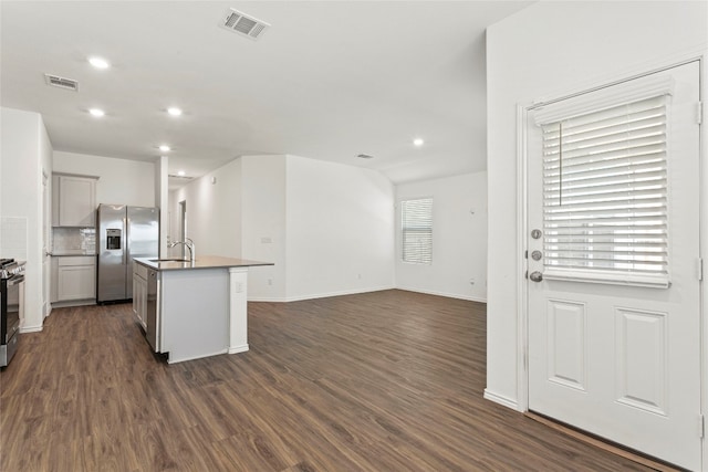 kitchen featuring sink, a kitchen island with sink, stainless steel appliances, dark hardwood / wood-style flooring, and decorative backsplash