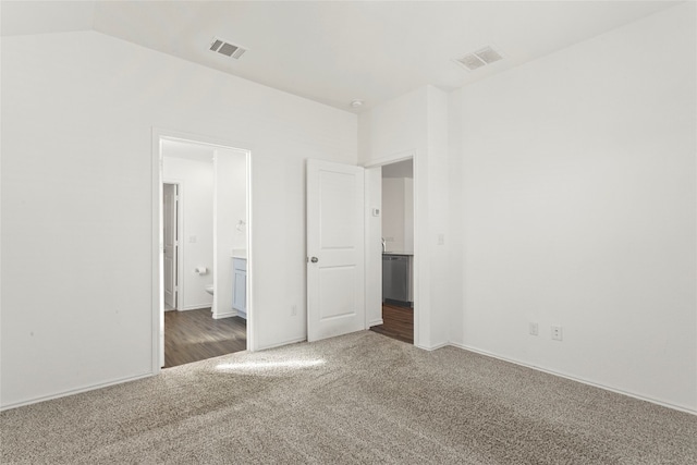 unfurnished bedroom with connected bathroom, lofted ceiling, and dark colored carpet