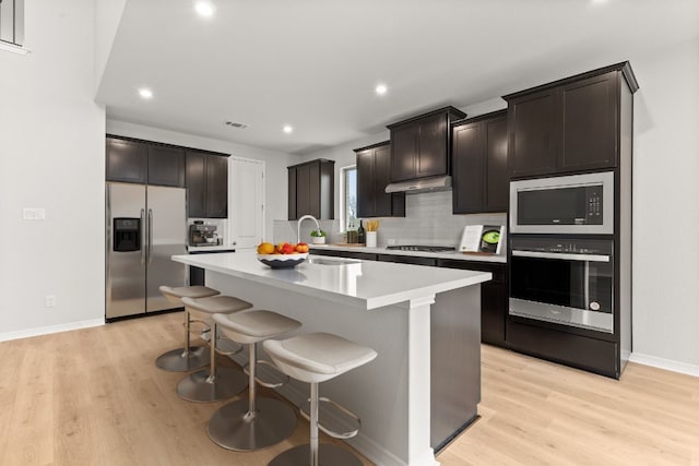 kitchen with appliances with stainless steel finishes, sink, a center island with sink, and light hardwood / wood-style floors