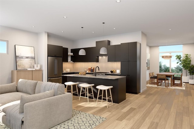 kitchen with high quality fridge, pendant lighting, a breakfast bar, a center island with sink, and light hardwood / wood-style flooring