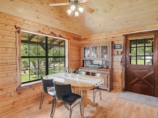 dining space with wood walls, light hardwood / wood-style flooring, ceiling fan, and high vaulted ceiling