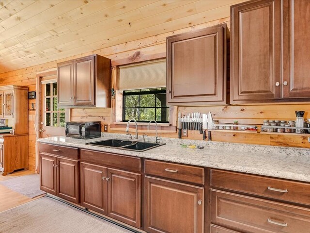 kitchen with light hardwood / wood-style flooring, sink, light stone counters, wood walls, and wooden ceiling