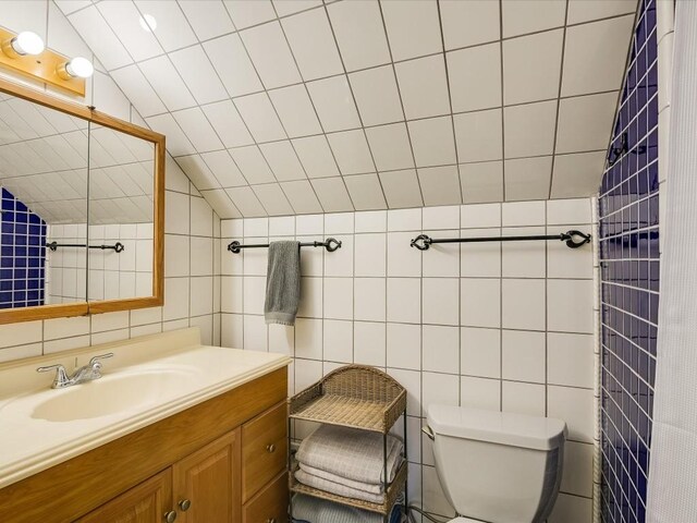 bathroom with vanity, tile walls, toilet, and vaulted ceiling