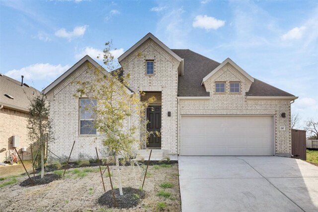 247 Du Bois Ln, Kyle, TX 78640 - french country home featuring a garage, brick siding, roof with shingles, and driveway