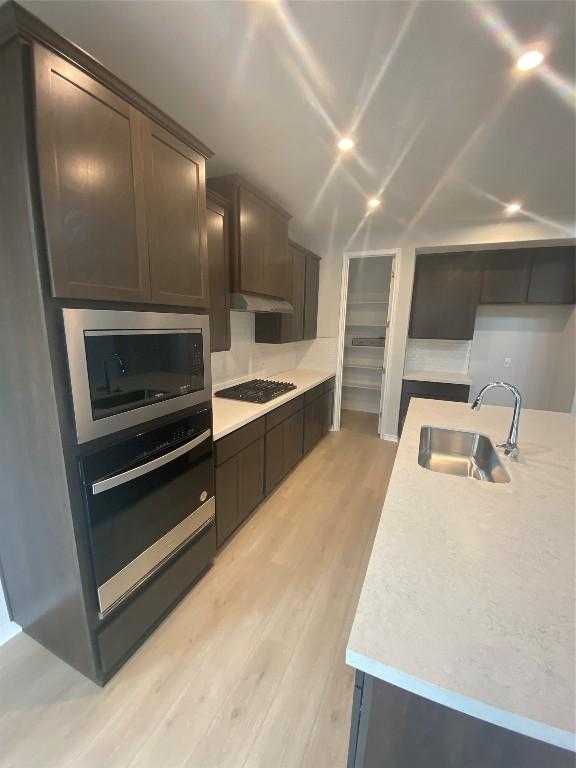 kitchen featuring built in microwave, sink, light wood-type flooring, oven, and black gas stovetop