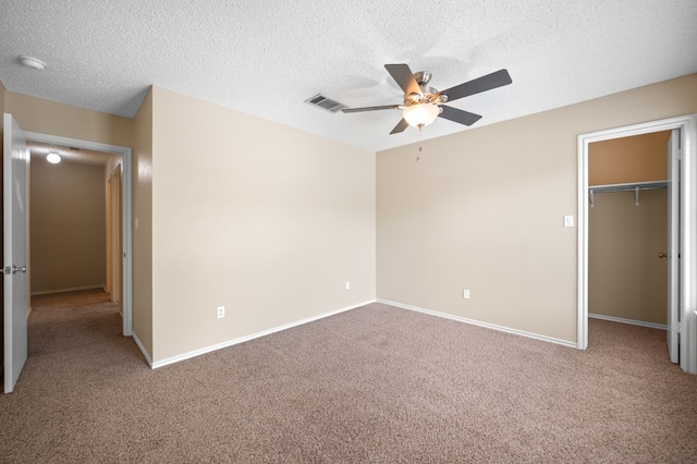 unfurnished bedroom with ceiling fan, a textured ceiling, a closet, a spacious closet, and light colored carpet