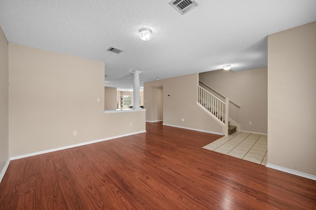 unfurnished living room with ornate columns, light wood-type flooring, and a textured ceiling