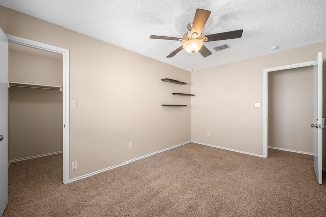 unfurnished bedroom with carpet floors, ceiling fan, a spacious closet, a closet, and a textured ceiling