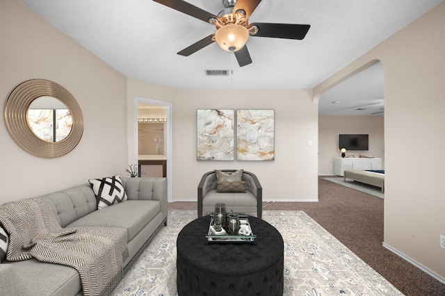 carpeted living room featuring ceiling fan and a textured ceiling