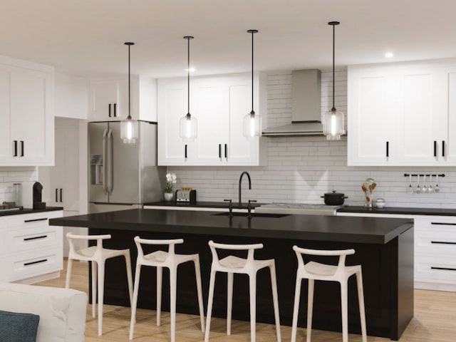 kitchen featuring decorative backsplash, an island with sink, wall chimney exhaust hood, a kitchen bar, and stainless steel fridge