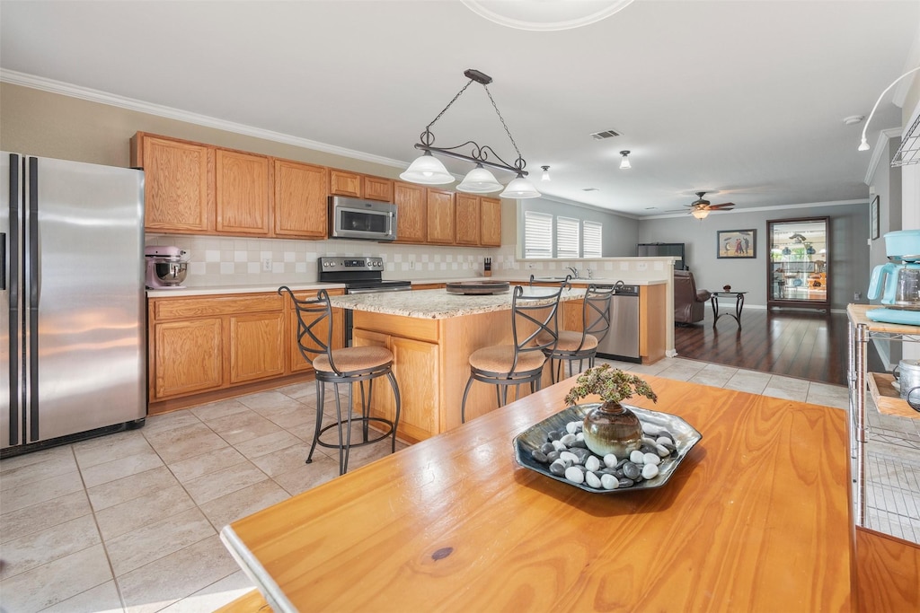 kitchen with pendant lighting, crown molding, ceiling fan, a kitchen island, and stainless steel appliances