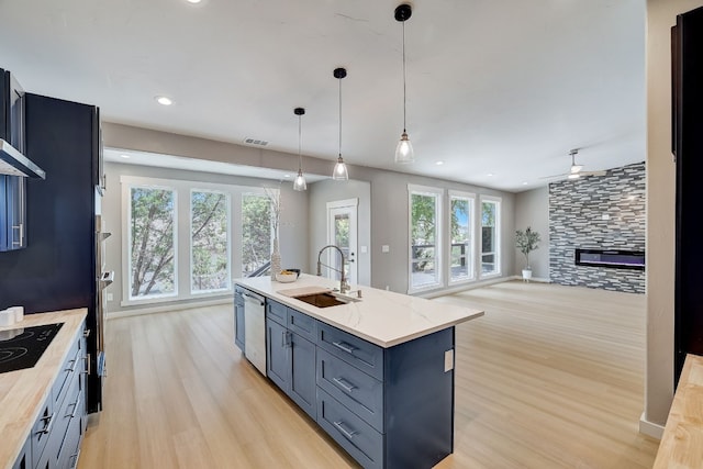 kitchen with an island with sink, light wood-type flooring, sink, stainless steel dishwasher, and decorative light fixtures