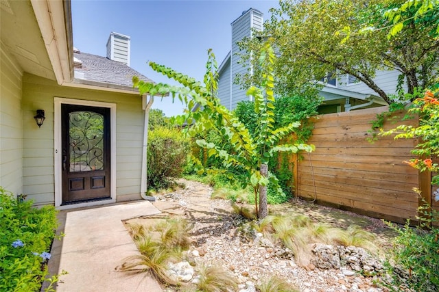 entrance to property with a shingled roof, fence, and a chimney