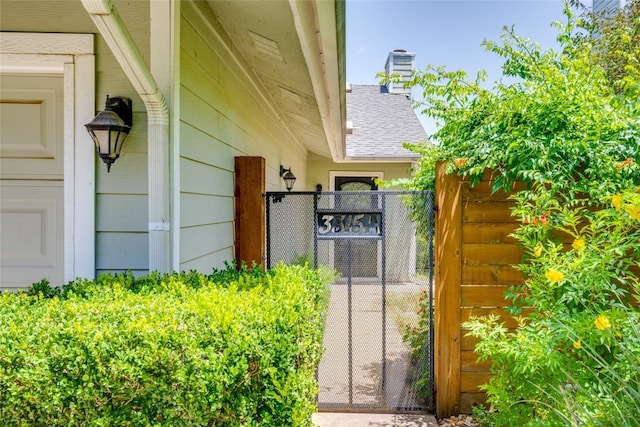 doorway to property featuring a gate, a chimney, and roof with shingles