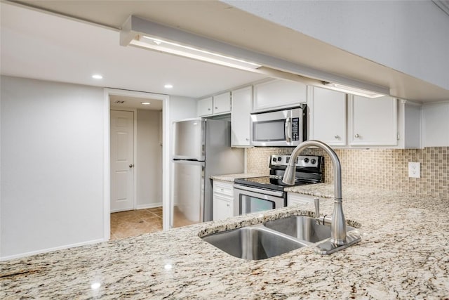 kitchen featuring light stone counters, a sink, white cabinetry, appliances with stainless steel finishes, and decorative backsplash