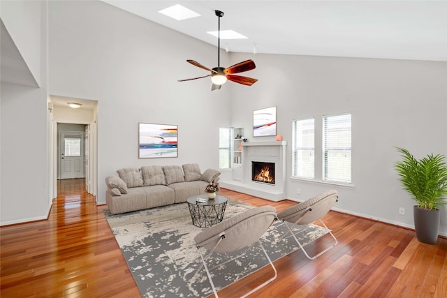 living room with wood-type flooring, ceiling fan, high vaulted ceiling, and a skylight