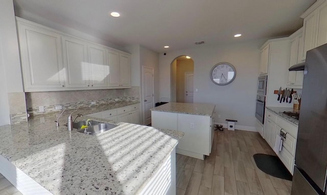 kitchen featuring oven, a peninsula, a kitchen island, a sink, and stainless steel microwave