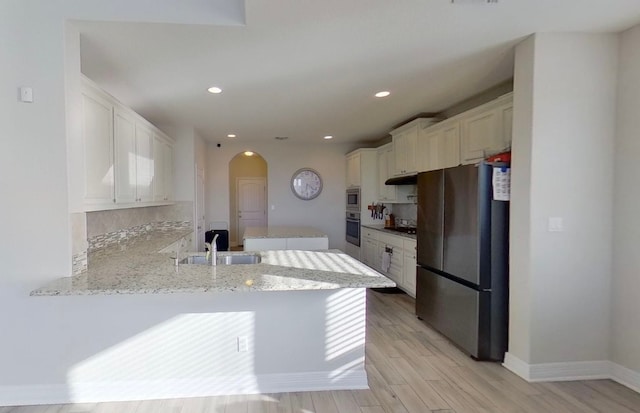 kitchen featuring appliances with stainless steel finishes, kitchen peninsula, sink, white cabinetry, and light wood-type flooring