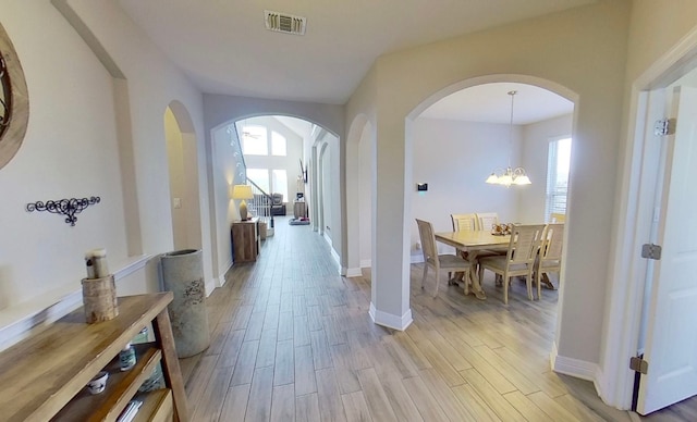 hallway with a wealth of natural light, an inviting chandelier, and light wood-type flooring