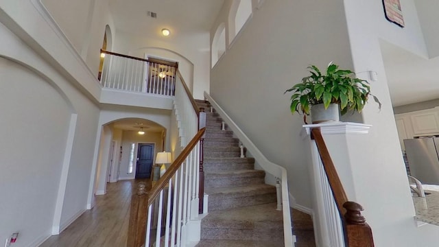 staircase featuring arched walkways, wood finished floors, visible vents, a towering ceiling, and baseboards